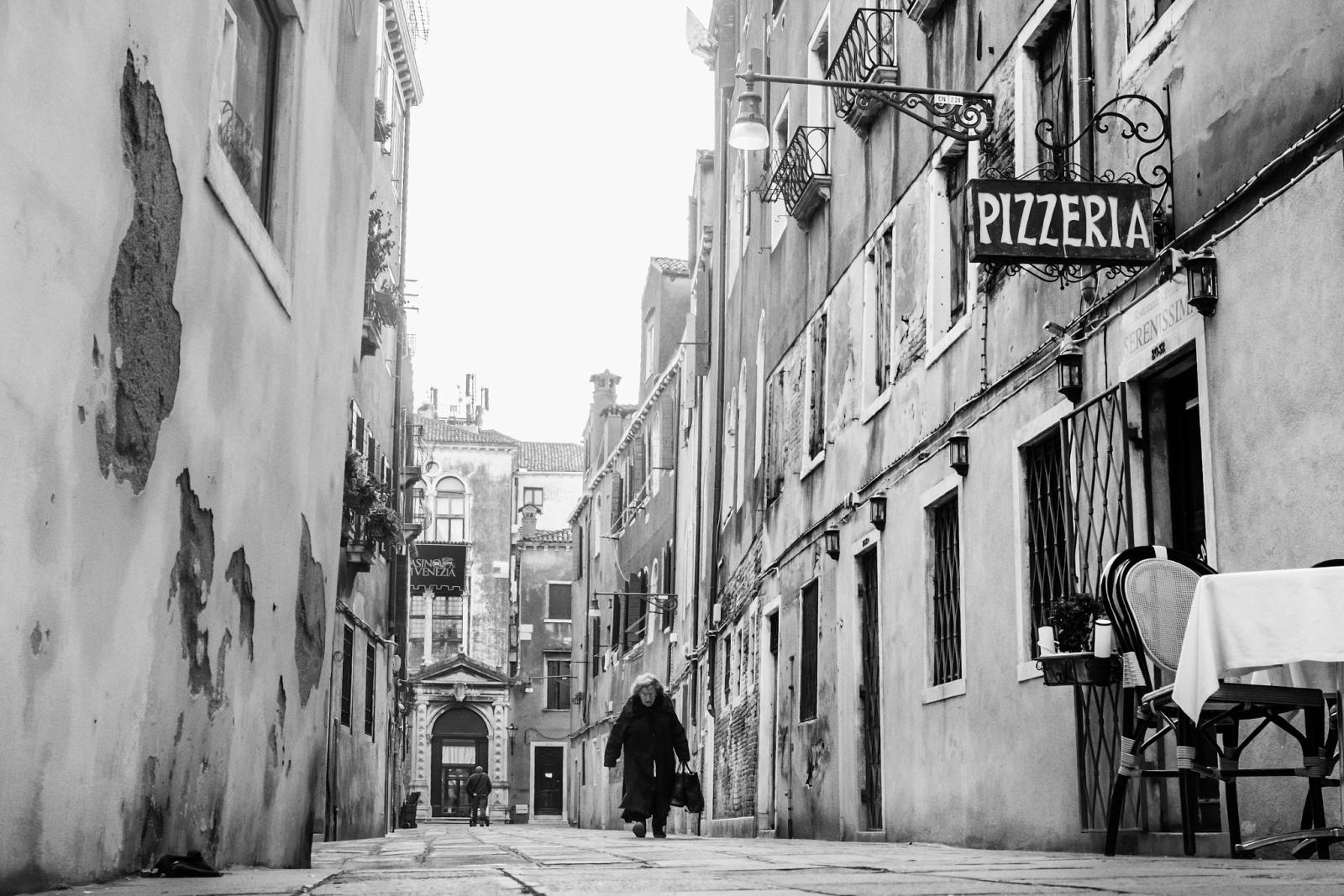 Una via stretta con l’insegna di una pizzeria, fotografia di Roberto Lugano