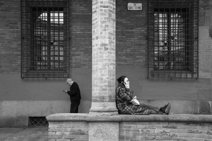Un uomo in piedi e una donna seduta sotto un portico di mattoni, fotografia di Roberto Lugano